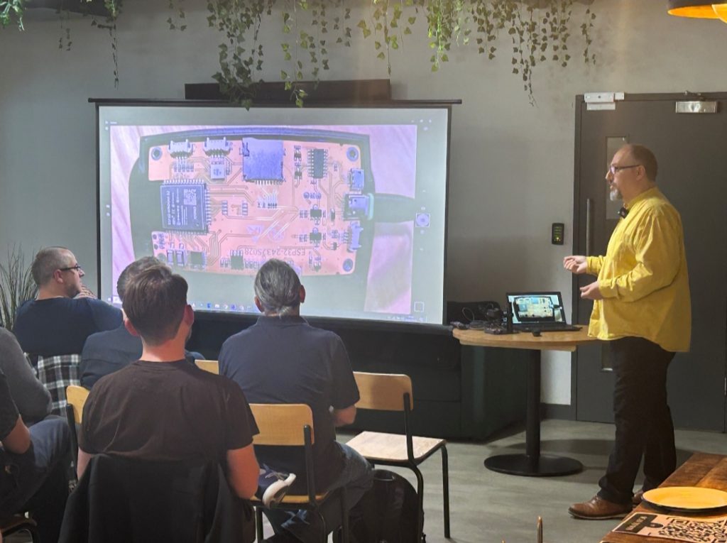 Andy explaining the Cheap Yellow Display to a bunch of Liverpudlian engineers and developers. A projector shows a close up of the board.
Photo credit: Josh Duxbury.